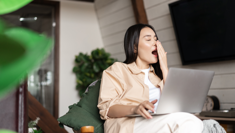 Kobieta ziewa podczas pracy na laptopie – typowy objaw, który może wskazywać na spadek energii po obiedzie.