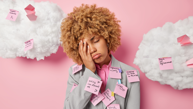 Kobieta przytłoczona obowiązkami z zamkniętymi oczami i karteczkami na ubraniu – symbolizująca zmęczenie psychiczne i przeładowanie informacjami.