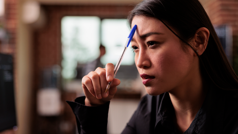 Kobieta zamyślona przy biurku, wspierająca głowę długopisem – symboliczne ujęcie trudności ze skupieniem, idealne do tematu "grzyby na koncentrację".