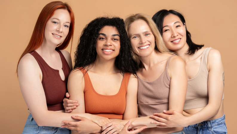 Cztery uśmiechnięte kobiety różnych narodowości wspierające się nawzajem – symbol siły, różnorodności i dbania o równowagę hormonalną kobiet.