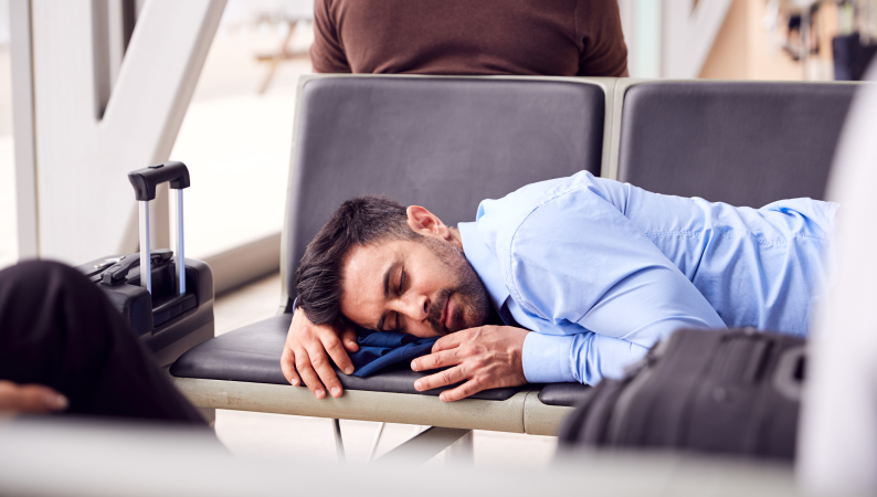 Mężczyzna śpiący na lotniskowej ławce po długim locie – melatonina na jet lag jako wsparcie w regulacji rytmu snu po podróży.
