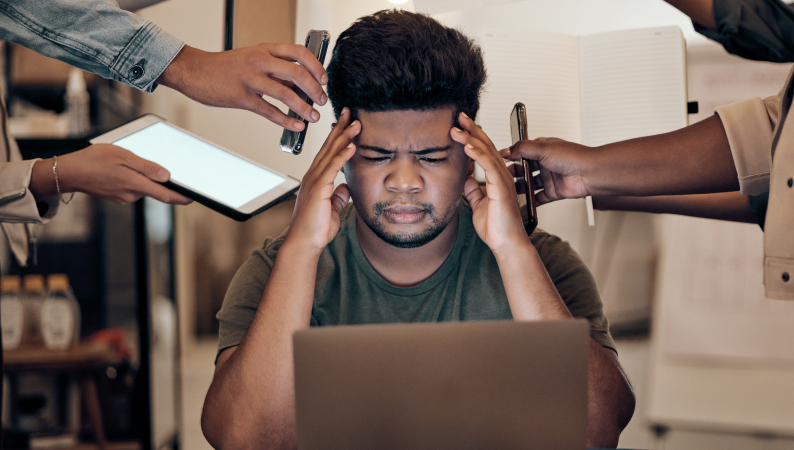 Mężczyzna przeciążony obowiązkami w pracy, trzyma się za głowę przed laptopem – ilustracja problemu, jakim jest stres w pracy zdalnej.