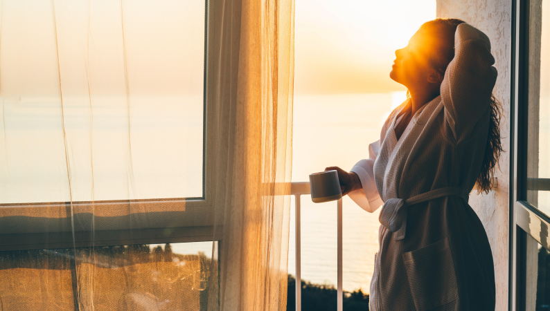 Poranny rytuał z adaptogenami – kobieta w szlafroku z kubkiem kawy lub herbaty, ciesząca się wschodem słońca i spokojnym początkiem dnia.