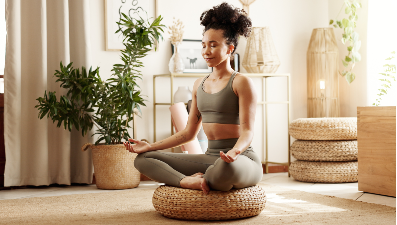 Kobieta medytująca w domu w otoczeniu roślin – ilustracja tematu wspieranie zdrowia psychicznego naturalnie poprzez uważność i relaks.